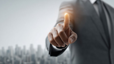 A focused businessman in a suit points confidently towards a city skyline, radiating a glowing effect that embodies innovation, leadership, and urban success.の素材