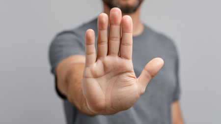 A man in a gray T-shirt displays an open hand gesture against a gray background, symbolizing stop, communication, and interaction in a casual setting.の素材