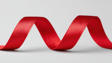 A vibrant red satin ribbon gracefully curves over a soft background, perfect for adding elegance to gifts, decorations, or creative projects during festive occasions.の素材