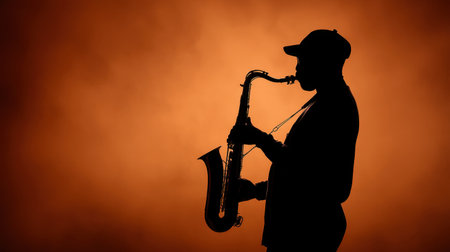 A striking silhouette of a saxophone player creates a mesmerizing scene with an orange backdrop and soft smoke, evoking emotion and artistic expression in music.の素材