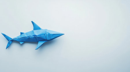 A vibrant blue origami shark crafted from paper, set against a light background. Perfect for themes related to ocean life, creativity, and minimalist design.の素材