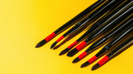 A vibrant arrangement of paintbrushes with black handles and red tips set against a bright yellow background, showcasing art tools for creative endeavors.の素材