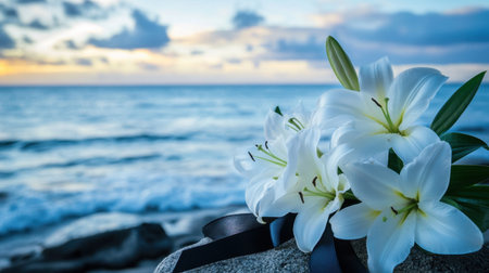 A stunning arrangement of white lilies rests on a stone against a backdrop of the serene ocean and a vibrant sunset, embodying tranquility and natural beauty.の素材