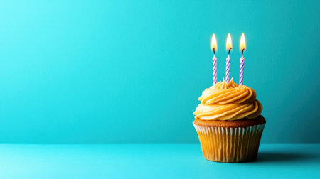 A delightful birthday cupcake with creamy yellow frosting topped with three burning candles against a vibrant turquoise background, perfect for festive celebrations.の素材