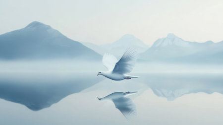 A graceful white bird soars over a calm mountain lake, reflecting the serene landscape. The scene captures a moment of tranquility and natural beauty.の素材