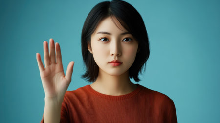 A serene portrait of a young woman raising her hand, conveying a sense of calm and communication against a vibrant blue background.の素材