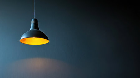 A sleek black pendant light emits a warm glow, providing an inviting ambiance against a dark wall. Ideal for modern interior design and decor.の素材