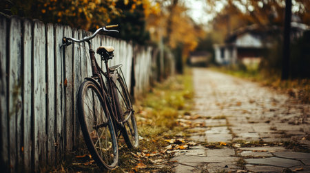 A serene autumn scene featuring a vintage bicycle resting against a weathered fence, surrounded by fallen leaves and a quiet path, evoking nostalgia and tranquility.の素材