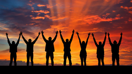 A group of people silhouetted against a stunning sunset, raising their arms in a joyful celebration of life and unity. The colorful sky adds warmth and inspiration.の素材