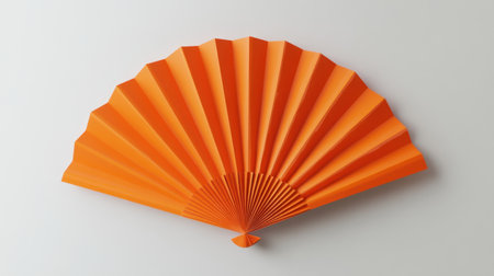 A vibrant orange paper fan elegantly pleated, showcasing a unique design. This decorative accessory creates a striking visual against a neutral background.の素材