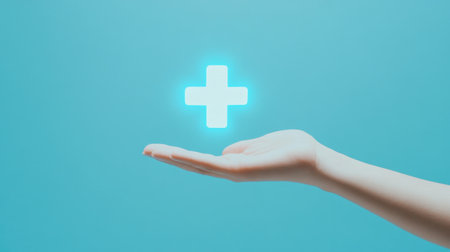 A hand holds a luminous plus sign, symbolizing support and health against a light blue background. This image is ideal for concepts related to care and wellness.の素材