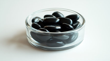 A clear bowl filled with smooth black pebbles on a white background, ideal for decorative purposes, meditation, or enhancing wellness experiences in a serene environment.の素材
