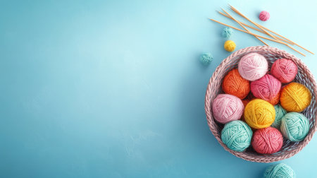 A woven basket filled with colorful yarn balls sits against a soft blue background, surrounded by knitting needles and small yarn bobbins, perfect for craft enthusiasts.の素材