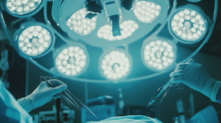 Close-up of gloved surgeon hands delicately maneuvering instruments under bright lights in a sterile operating room.の素材