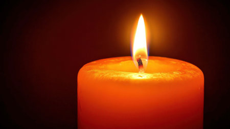 This image captures a close-up view of an orange candle flame, radiating warm light in a dark setting, perfect for creating a peaceful ambiance for various occasions.の素材