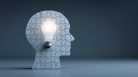 This creative illustration features a human head silhouette made of puzzle pieces, with a bright light bulb at its center, symbolizing innovative ideas and thinking.の素材