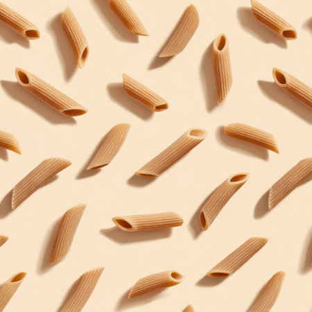 This image features raw penne pasta dispersed elegantly over a soft cream background, emphasizing its unique texture and shape ideal for food presentations and cooking recipes.の素材