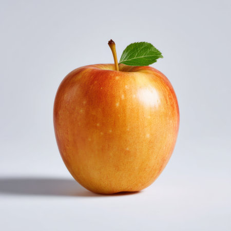 This image features a fresh red apple with a green leaf, set against a light grey background. Ideal for promoting healthy eating and natural food themes.の素材