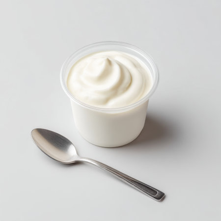 A clear plastic cup filled with creamy yogurt placed beside a silver spoon. This image highlights a healthy snack option, perfect for various culinary uses.の素材
