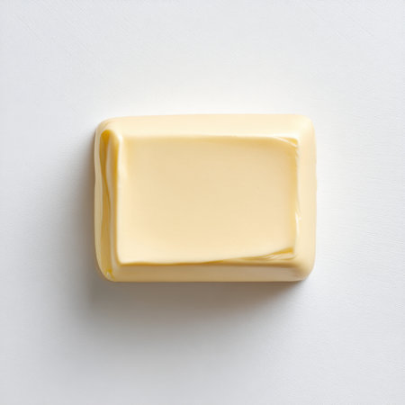 A smooth and creamy block of butter rests on a white surface, ideal for food photography. Perfect for showcasing culinary applications and cooking inspirations.の素材