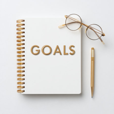 A clean, stylish flat lay featuring a white notebook with 'GOALS' in gold letters, accompanied by elegant gold-rimmed glasses and a pen, perfect for motivation.の素材