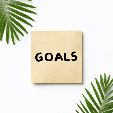 A simple sticky note displaying the word "GOALS" in bold letters, complemented by fresh green leaves on a clean white background. Ideal for motivation.の素材