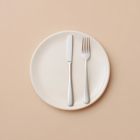 A minimalist arrangement featuring a white plate with a silver fork and knife positioned neatly on a soft beige background, ideal for culinary presentations.の素材