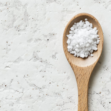This image features granules of sea salt displayed on a wooden spoon against a light textured background, ideal for culinary, health, and cooking-related themes.の素材