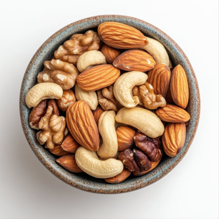 An inviting display of assorted nuts including almonds, cashews, walnuts, and pecans in a ceramic bowl positioned on a clean white background, perfect for healthy snack ideas.の素材