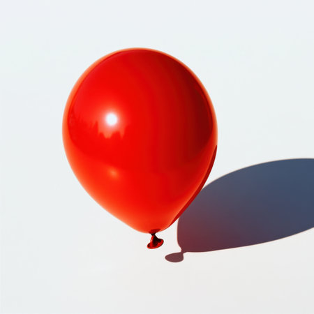 A bright red balloon floats gently against a minimalistic white background, casting a soft shadow and evoking feelings of joy and celebration in any context.の素材