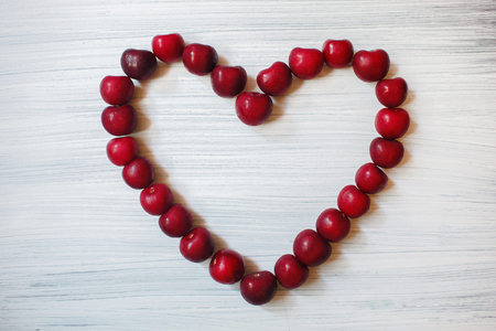 Heart made of dark cherries. Red fruit on wooden background. Summer sends love. Particles of art.の写真素材