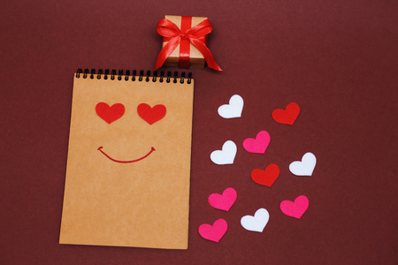 The 14th of February. Valentines Day. Holiday concept. Pictured is a notebook with hearts and a smile, next to it is a wrapped gift.の写真素材