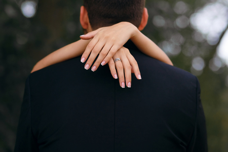 the girl embraces the neck of the groom, the beautiful bride walks in the park with the groom, on her finger ringの写真素材