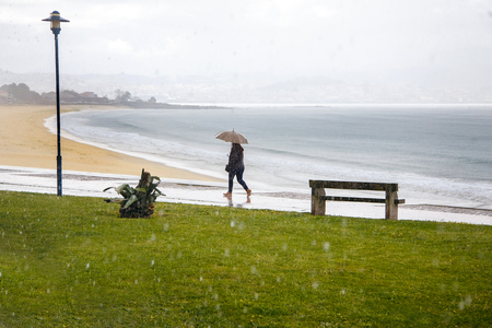 a woman with an umbrella is walking along the embankment, it is raining, the Atlantic Ocean, bad weather.の写真素材