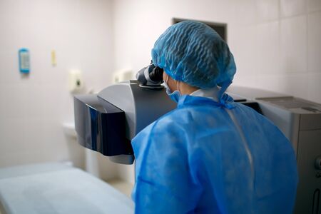 Woman doctor sits at his workplace and looks through a microscope, a scientist works, an eye doctor.の写真素材