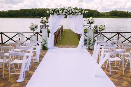 Wedding. Ceremony. Wedding arch. Wedding arch made of branches, flowers and greenery is on the green grass on the river bankの写真素材