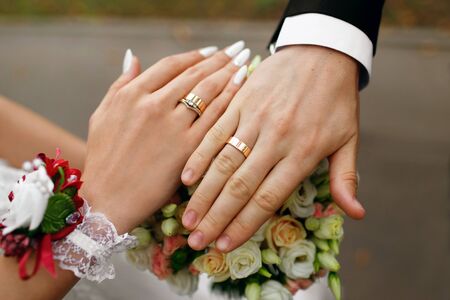 Hands of the newlyweds with rings on their fingers, near a bouquet of roses, the bride and groom...