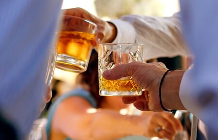 a fun company celebrates, clinks glasses, drinks whiskey with ice, golden cognac, two glasses of...