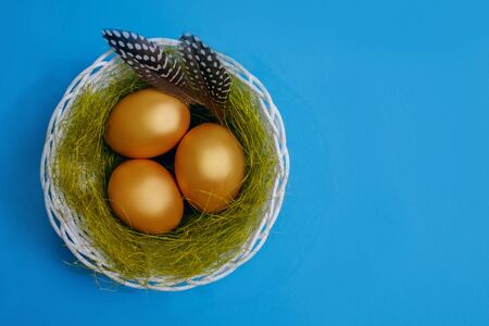 Golden easter eggs lie in a nest with quail feathers on a blue background, easter compositionの写真素材