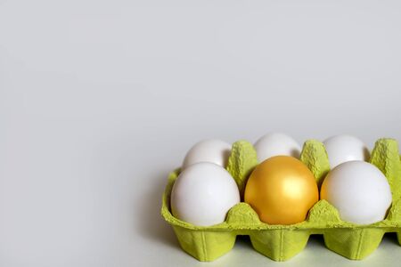 Chicken golden egg with white eggs in a box on white. Conceptual photo of team leadership. The best specimen surrounded by ordinary objects, Easterの写真素材