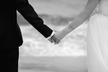 black and white photo of newlyweds, bride and groom holding each other's hands with rings, happy man and woman hold each other's hands on the background of the oceanの写真素材