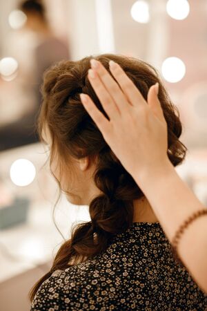 Hairdresser makes hairstyle to a girl in the salon, stylish interior in the beauty salon, professional hairdresser, braiding hair close-up, view from the back, women's clubの写真素材