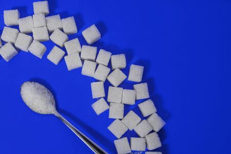 spoon of sugar on a blue background with pieces of sugar, sugar as a taste or harmful substance, diabetes mellitus, free space for textの写真素材