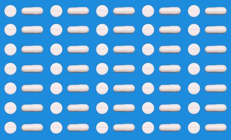 On a blue background, two types of tablets are presented: white round and oblong capsules. The concept of medicine, treatment of diseasesの写真素材