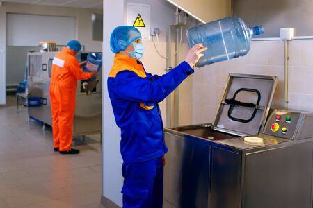 Drinking water treatment plant, factory workers wash large plastic bottles and pour water into containersの写真素材
