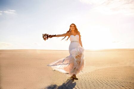 beautiful bride in a white wedding dress walks in the sandy desertの写真素材
