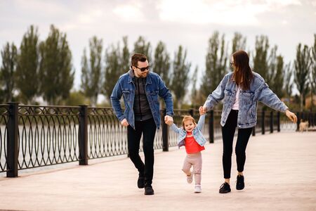A young, fashionable family walks along the embankment of the river, mom and dad hold daughters handsの写真素材