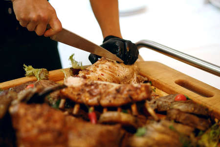 the cook in the restaurant cuts the meat cooked on the fireの写真素材