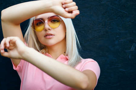 blonde in colored sunglasses on a black background of boards looks from above and poses for the photographerの写真素材