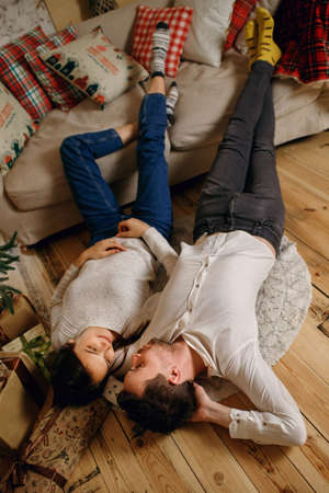 The lovers celebrate the New Year together. A man and a woman lie on the floor near the Christmas tree and gifts.の写真素材